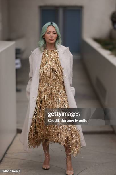 Tina Leung seen wearing diamonds earrings, a gold fringed halter neck short dress, rhinestones necklace, gold large chain bracelet, white creme...