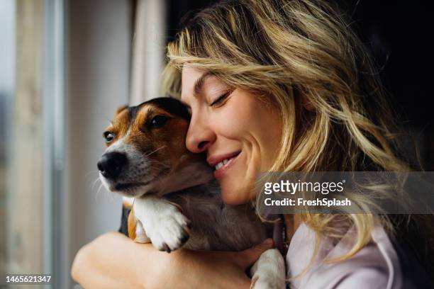 a happy beautiful blonde woman hugging her cute dog while keeping her eyes closed - smiling brown dog stock pictures, royalty-free photos & images