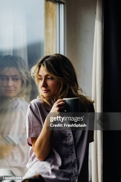 eine glückliche schöne blonde frau im schlafanzug, die nachdenkt, während sie ihren morgenkaffee genießt - trennungsschmerz stock-fotos und bilder