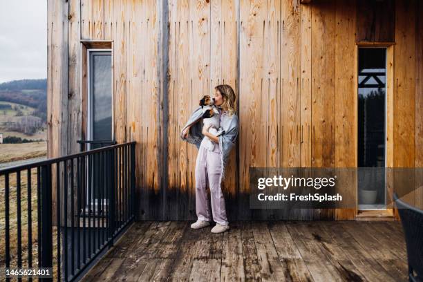 a happy beautiful blonde woman covered with a blanket kissing her cute dog while keeping her eyes closed - dog eyes closed stock pictures, royalty-free photos & images