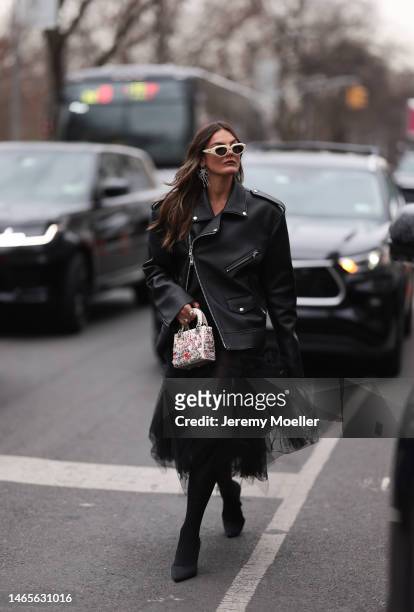 Tezza Barton seen wearing Bottega Veneta beige sunglasses, silver statement earrings, a black shiny leather zipper oversized jacket, Lady Dior white...