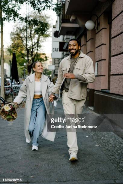 couple running down city street laughing and holding hands - couples romance stock-fotos und bilder