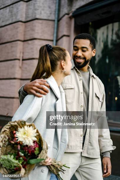 boyfriend with arm around his girlfriend's shoulder walking down city street - engagement stock pictures, royalty-free photos & images