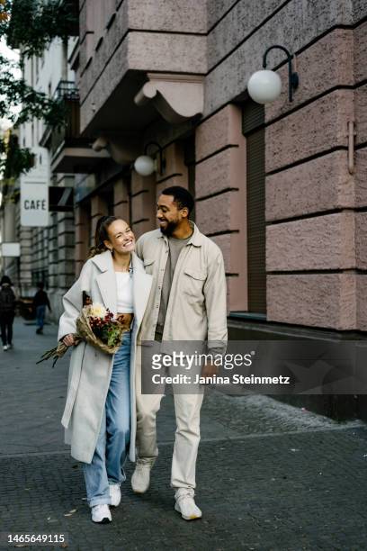 couple walking down city sidewalk with arms around each other - young couple stock-fotos und bilder