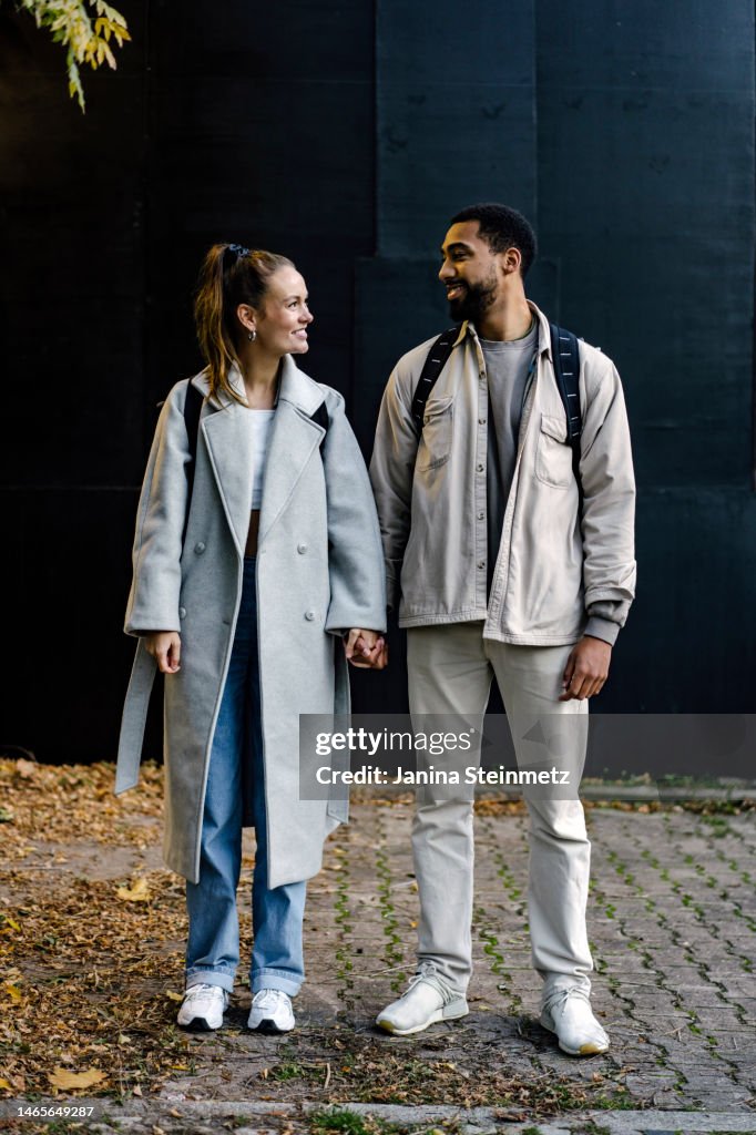 Full length portrait of couple holding hands and looking lovingly at each other
