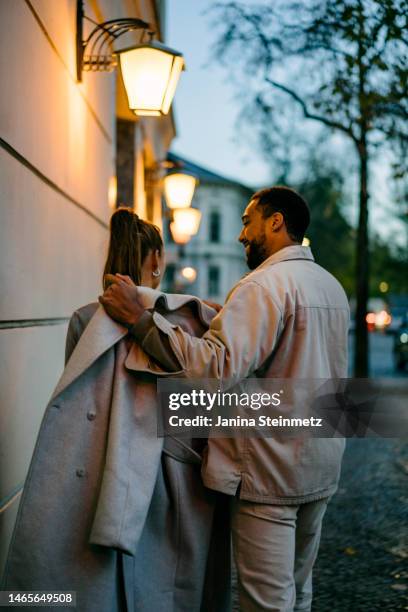 man putting trench coat on woman's shoulders at night - etiquette stock-fotos und bilder