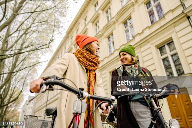close up of two young adult women pushing their bicycles and walking through the city - travel stock-fotos und bilder