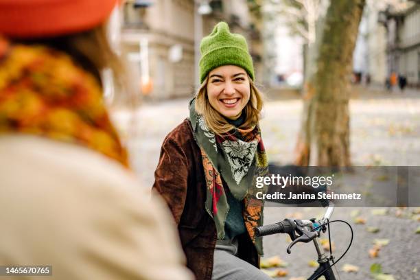 young adult female smiling at friend on city street - jahreszeiten stock-fotos und bilder