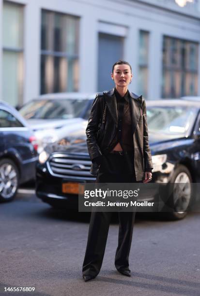 Amalie Gassmann wears a black shiny leather blazer jacket, black lace blouse shirt, a black shiny leather belt, black suit pants, a black shiny...