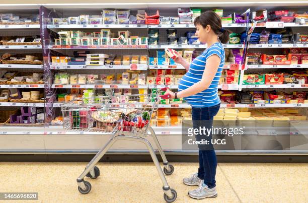 Pregnant woman checking label on cheese at Sainsbury's supermarket, England, UK.
