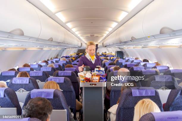 Monarch Airlines air steward serving snacks from the drinks trolley, England, UK.