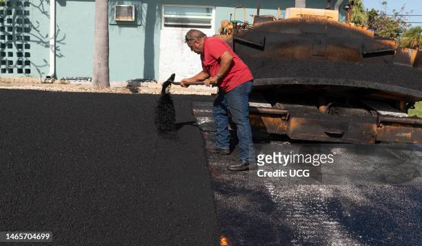 Cocoa Beach, Florida, Asphalting worker using a shovel to spread the Asphalt material to level before rolling operation.