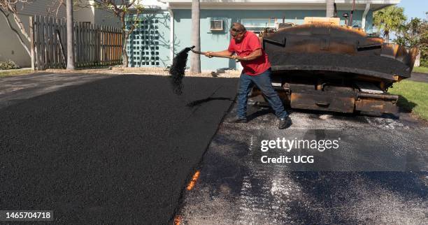 Cocoa Beach, Florida, Asphalting worker using a shovel to spread the Asphalt material to level before rolling operation.