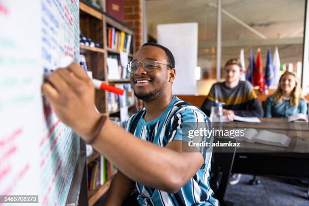 junger schwarzer männlicher college-student, der notizen an eine weiße tafel schreibt - master stock-fotos und bilder
