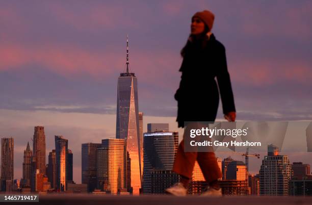 The sun sets on the skyline of lower Manhattan and One World Trade Center in New York City as a womam walks in a park on February 13 in Jersey City,...