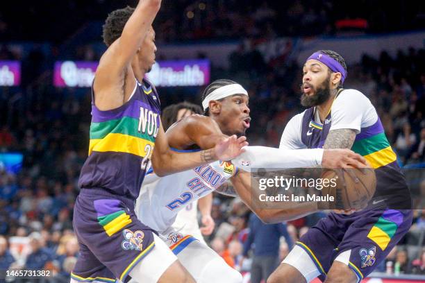 Shai Gilgeous-Alexander of the Oklahoma City Thunder drives past Trey Murphy III of the New Orleans Pelicans and Brandon Ingram of the New Orleans...