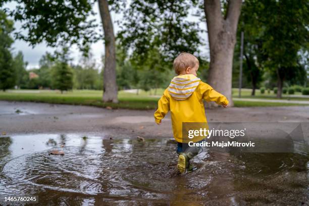 little boy walking outdoors and jumping on puddle - puddle splashing stock pictures, royalty-free photos & images