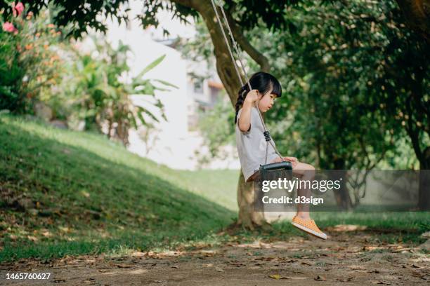 little asian girl looking down while playing on the backyard swing alone, looking sad and lonely on her face. the importance of parents accompany as the child grow - asian waiting angry expressions stock pictures, royalty-free photos & images