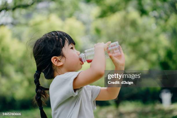 side profile of hot and sweaty little asian girl drinking a bottle of fruit juice in the park outdoors on a hot summer day - overheated stock pictures, royalty-free photos & images