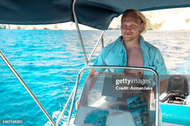 adult caucasian blonde male boat owner enjoying driving a boat on his vacations - beard pilot stock pictures, royalty-free photos & images