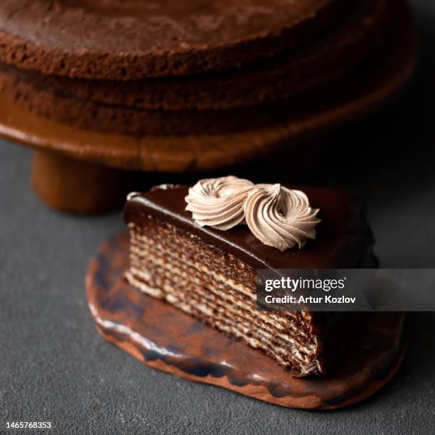 piece of chocolate cake with butter cream. dessert on ceramic plate. cake layers on stand in background. dark background. soft focus. copy space. top view - party pies foto e immagini stock