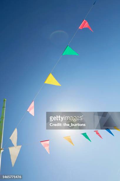 colorful bunting flags/ pennant chain for party decoration against sky and sun - pennant stock pictures, royalty-free photos & images