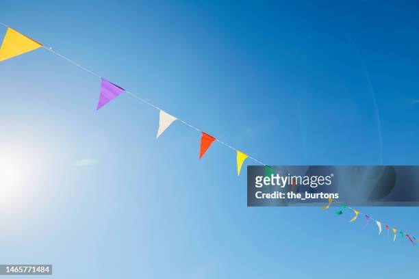 colorful bunting flags/ pennant chain for party decoration against sky and sun - 旗　三角 ストックフォトと画像