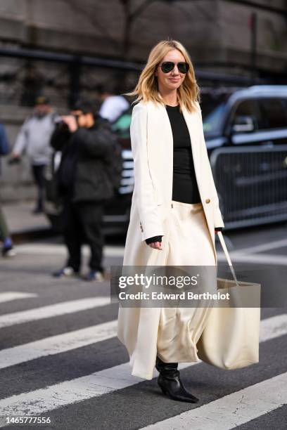 Lisa Aiken wears black sunglasses, a black t-shirt, a white latte long coat, beige silk long skirt, a beige shiny leather handbag, black shiny...