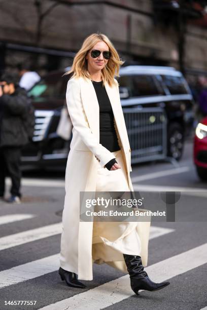 Lisa Aiken wears black sunglasses, a black t-shirt, a white latte long coat, beige silk long skirt, a beige shiny leather handbag, black shiny...