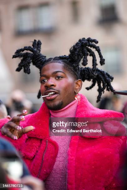 Lil Nas X wears red pendant earrings, a pink glitter wool turtleneck pullover, a red fluffy oversized long coat, outside Coach, during New York...