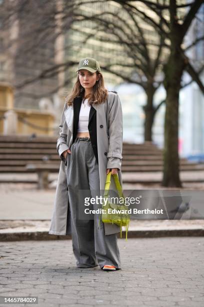 Iana Rad wears a pale khaki denim with embroidered white logo cap from New Era, a white cropped top, a black blazer jacket, a pale gray long coat,...