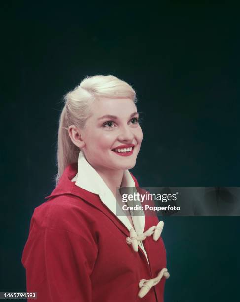 Posed studio portrait of Australian actress Diane Cilento wearing a red duffel coat, London, 1954.