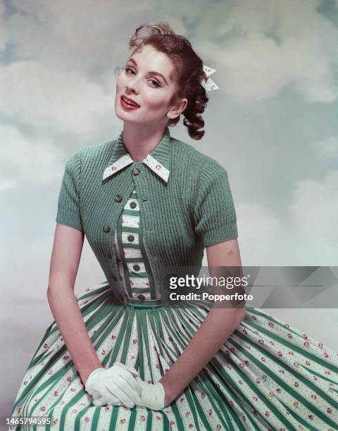 Posed studio portrait of a woman wearing a cotton dress with green stripes under a shortie jacket and white gloves, London, 1st June 1957.
