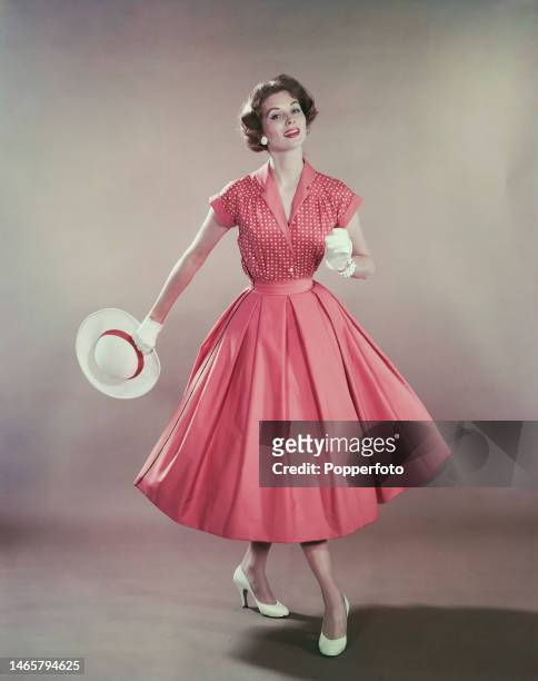 Posed studio portrait of a woman wearing a pink patterned short sleeved blouse with contrasting plain pink collar and cuffs, and a matching pink...
