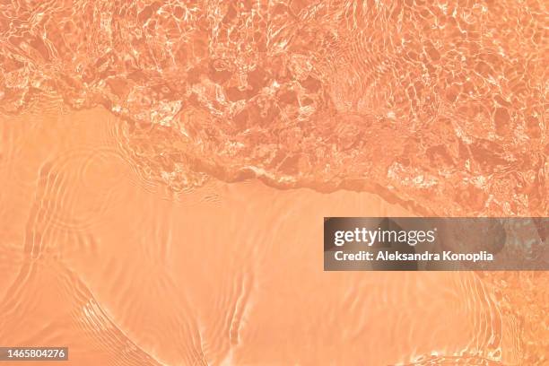 light pastel coral peach orange transparent clear water surface texture with ripples, splashes and waves in sunlight - de color melocotón fotografías e imágenes de stock