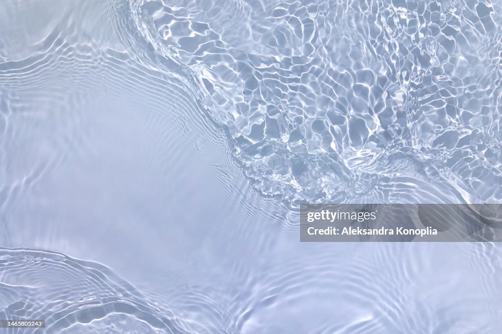 Light pastel blue transparent clear water surface texture with ripples, splashes and waves in sunlight