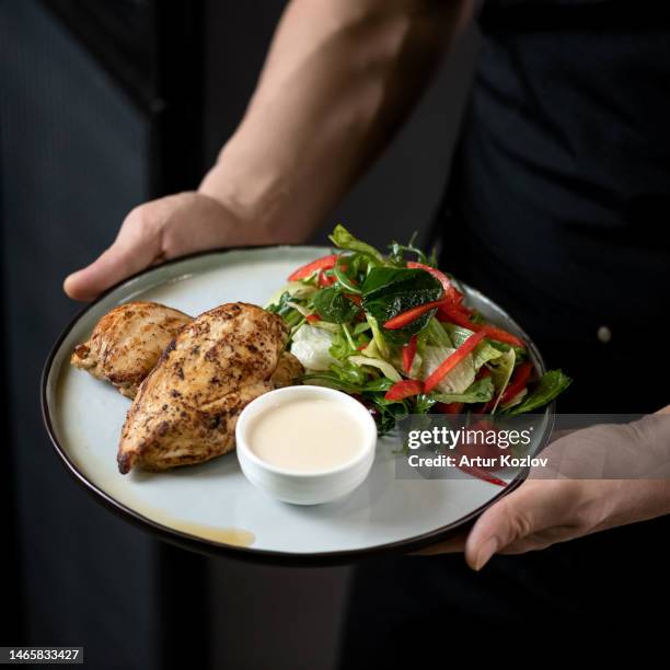 baked chicken breast with fresh vegetable salad and sauce. dish on white plate in hands of cook. healthy diet. fitness menu. low calorie food. view from above. soft focus - cooked turkey white plate stockfoto's en -beelden