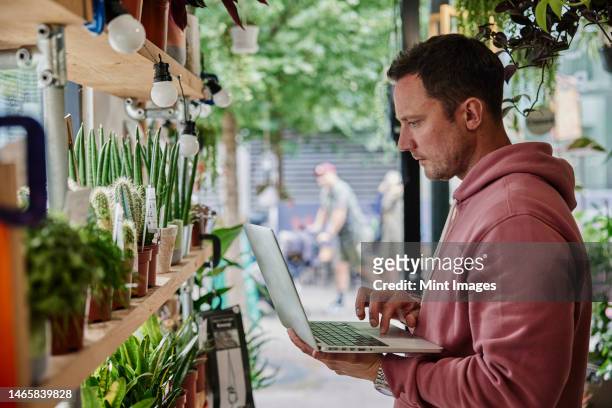 man stock-taking using laptop in flower shop - recycled plant pot stock pictures, royalty-free photos & images