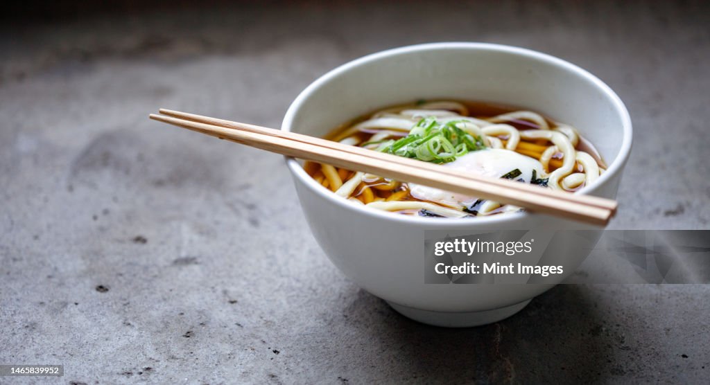 A bowl of noodles, vegetables and broth and a set of chopsticks
