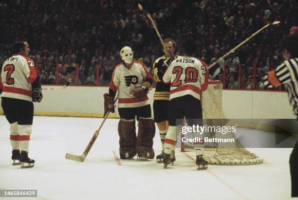 As Philadelphia goalie Bernie Parent guards the net, teammate Jimmy Watson and Boston's Wayne Cashman swing their hockey sticks in the fourth game of...