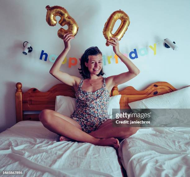 30 years birthday celebration. sitting in bed and holding up inflatable balloon 30 sign with a happy birthday garland - 30 34 years bildbanksfoton och bilder