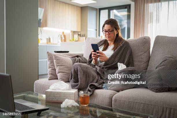 femme malade tenant un téléphone sur le canapé - maladie photos et images de collection