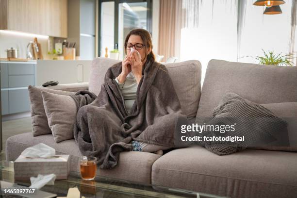 sick woman blowing her nose sitting on sofa at home - covering cough stock pictures, royalty-free photos & images