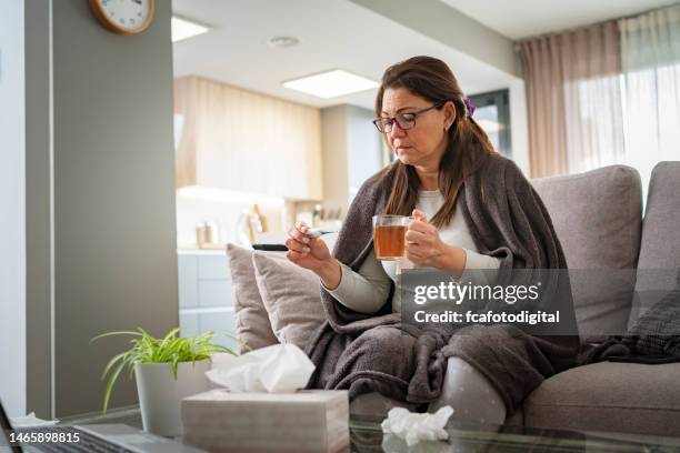 sick woman checking her temperature and holding tea cup - covering nose stock pictures, royalty-free photos & images