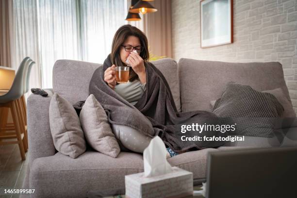 woman suffering flu blowing her nose and holding a hot tea cup - sinusitis stock pictures, royalty-free photos & images
