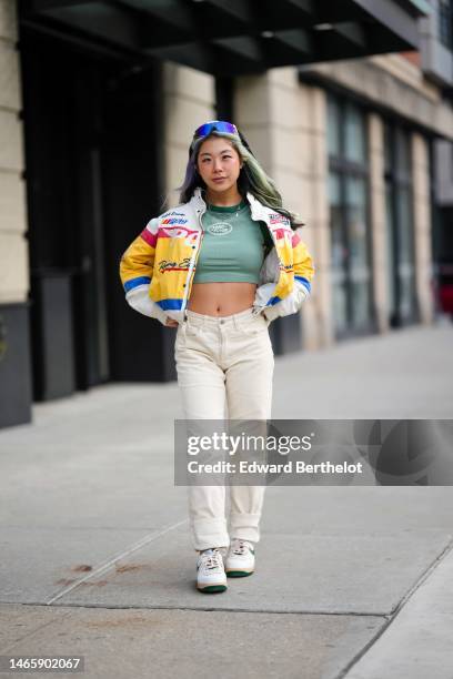 Guest wears blue and purple futurist sunglasses, a silver chain pendant necklace, a green with white print pattern cropped t-shirt from Land Rover, a...