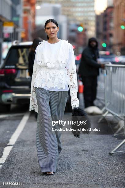 Guest wears a white with embroidered and cut-out flower blouse, gray striped print pattern large wide legs pants, a black fluffy handbag , outside...