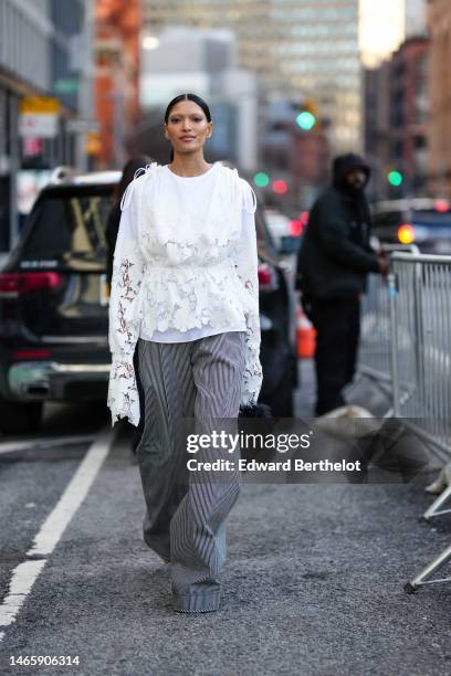 Guest wears a white with embroidered and cut-out flower blouse, gray striped print pattern large wide legs pants, a black fluffy handbag , outside...