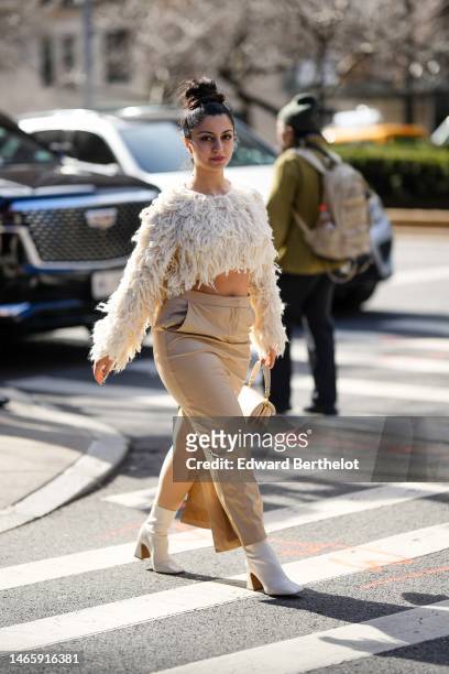 Guest wears a white fluffy cropped top, a beige long skirt, a beige matte leather puffy handbag from Coach, white shiny leather block heels ankle...