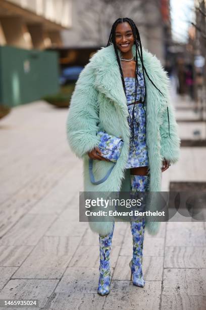 Guest wears silver and rhinestones earrings, a diamonds necklace, a pale green long oversized fluffy long coat, a white with blue and green flower...